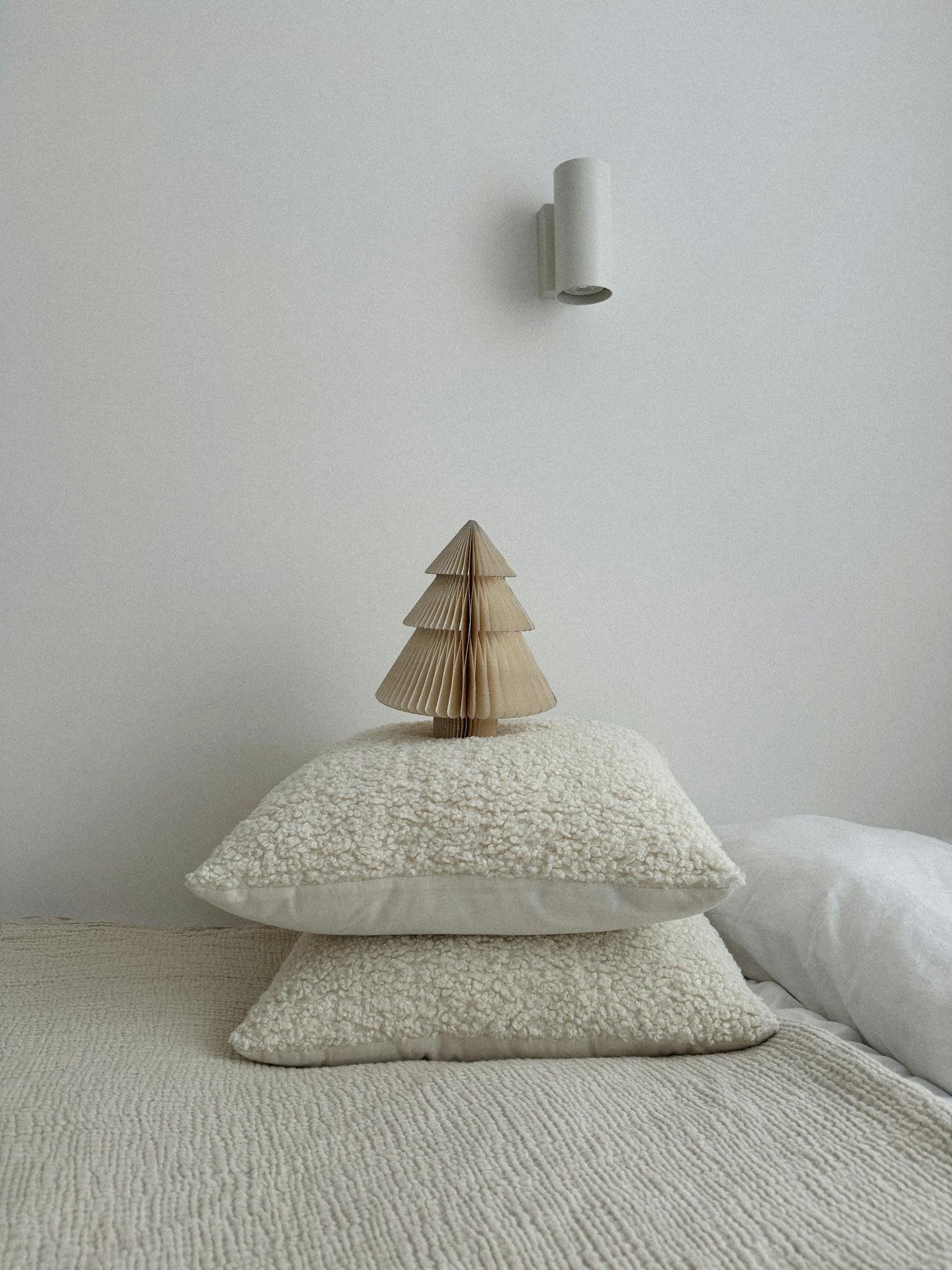 Simple and cozy bedroom scene featuring minimalist decor with pillows and a tree ornament.